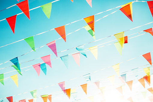 Colorful celebration with multi-colored flags and buntings hanging under clear sky.