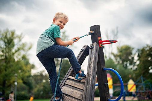 Portrait of little boy climbing in the playground on an overcast autumn day.