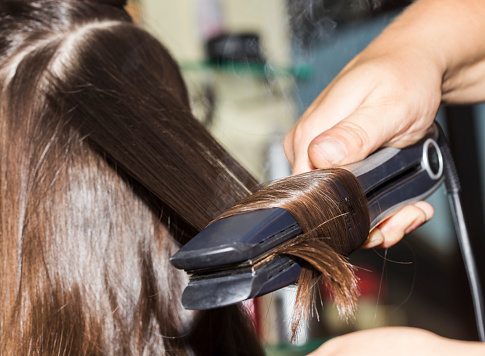 Close-up of a hairdresser making curles with brown hair.
