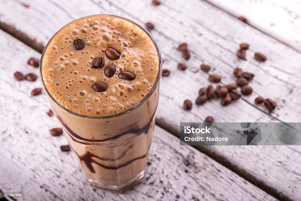 Cold chocolate milkshake frappe in tall glass with ice Cold chocolate milkshake frappe in tall glass with ice on white wood background Coffee - Drink Stock Photo