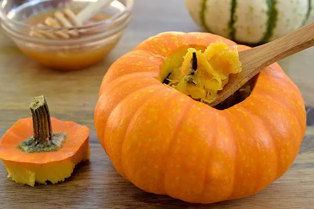 Two baked mini-pumpkins stuffed with spiced pumpkin puree, served with honey, on green dishcloth and wooden table, viewed from above- seasonal food concept