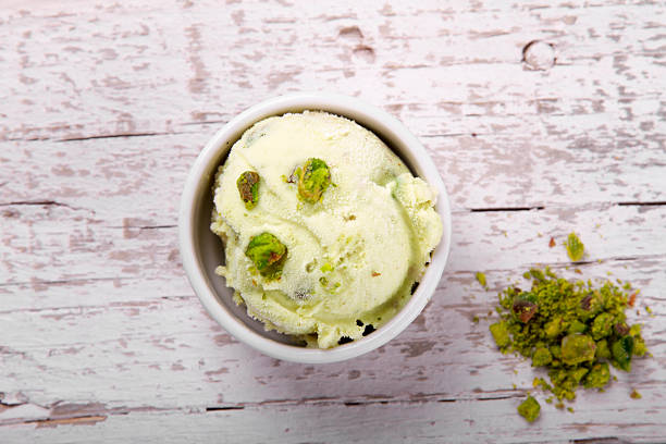Scoop of pistachio ice cream in bowl on white wood