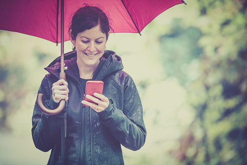 DSLR picture of a Woman with red umbrella and using a smart phone on a rainy day.