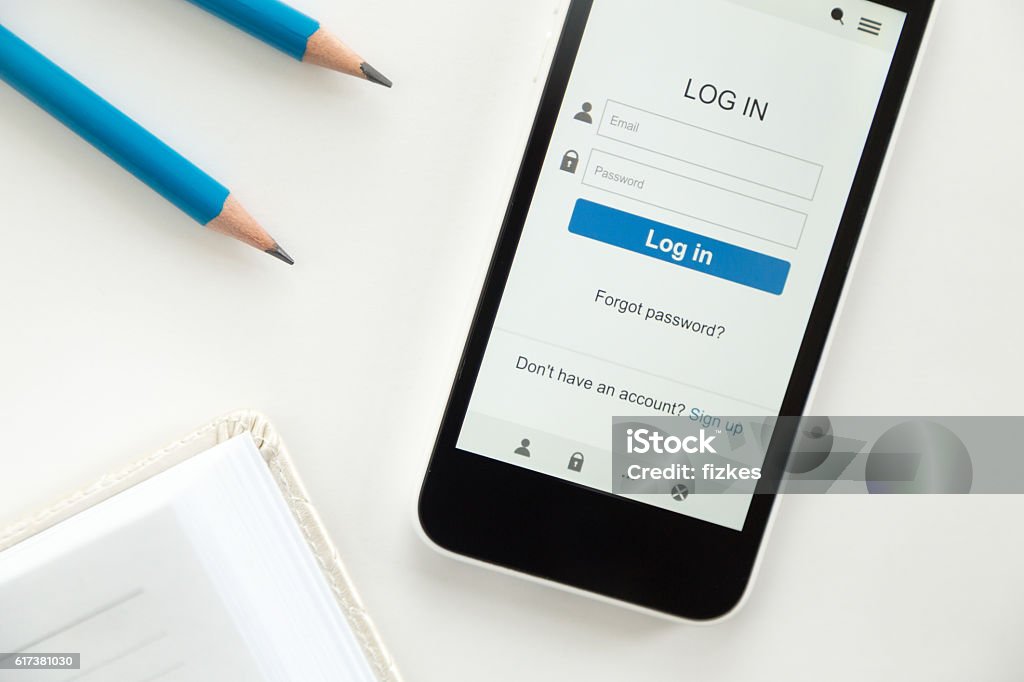 Top view a phone on desk, log in on screen Top view of a mobile phone lying on a white office desk, log in on the screen, part of a notebook, sharp pencils, blue color. Business concept, lay flat Log On Stock Photo