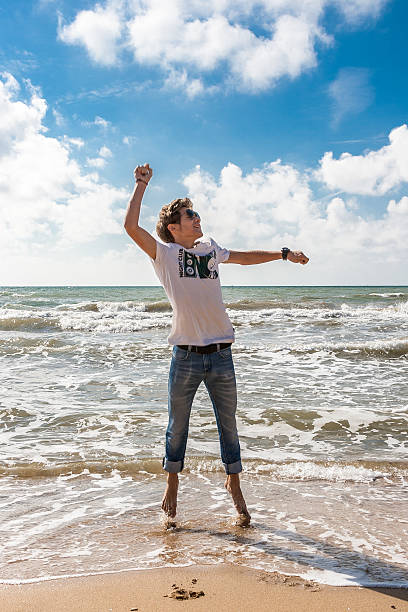 istock Young man jumping on the beach in the oncoming waves 617393768