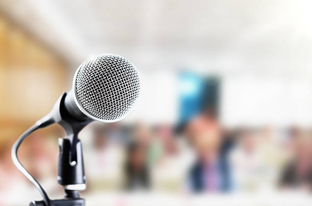 istock High-key mic with defocused seated audience in background 617567330