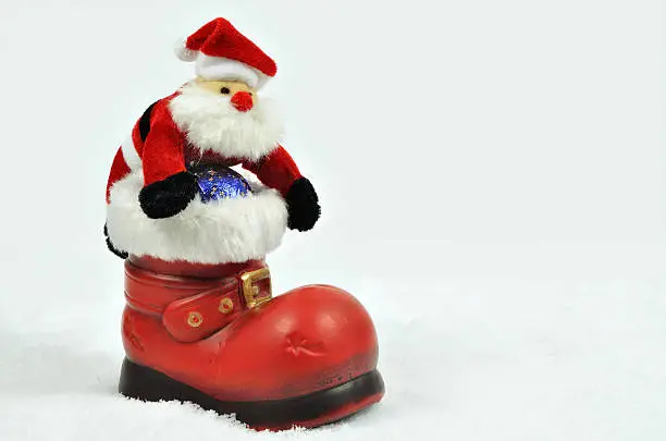 Santa Claus with sweets inside a red boot with white fur trimming on snow background, close up, space for text, horizontal
