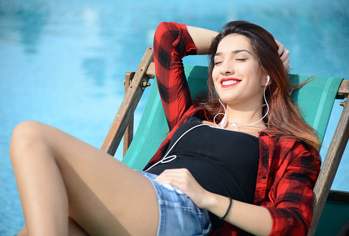 happy beautiful young woman relaxing  by the swimming pool with ear bud