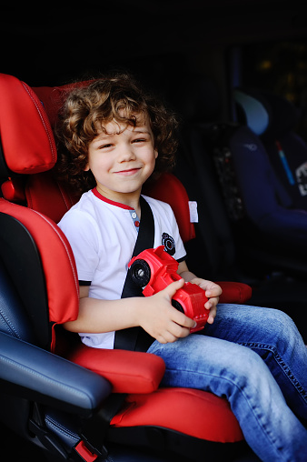 baby boy with curly hair sitting in red car seat in the cabin minibus