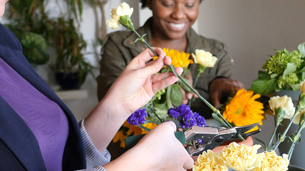 Young Caucasian and African American female florist work in a flower shop. They are creating floral arrangements for customers. They are using a variety of flowers.