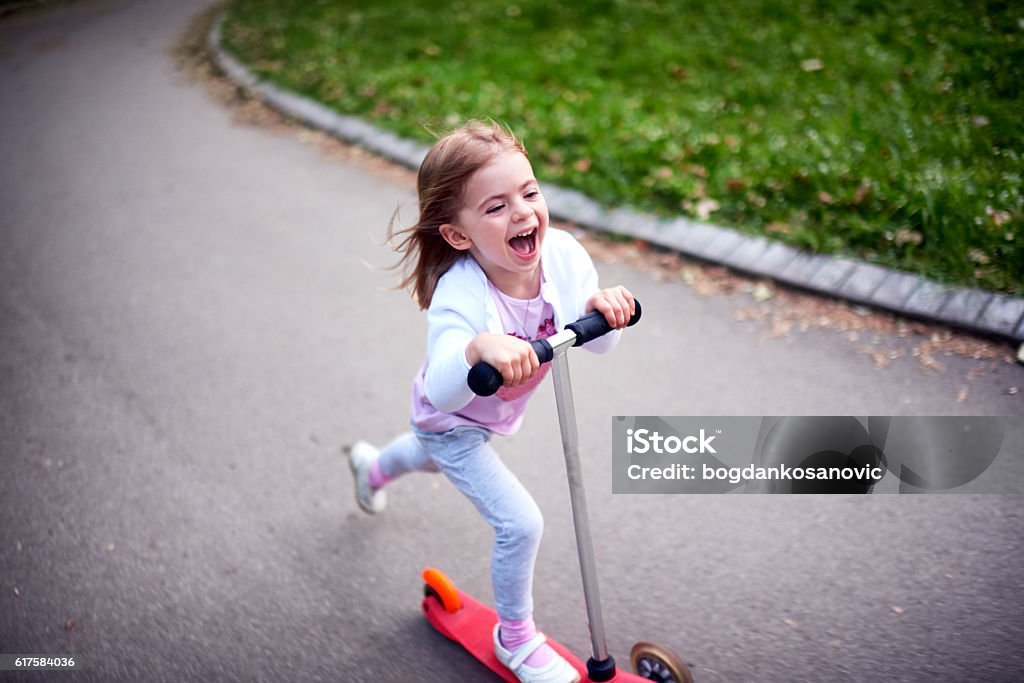 Girl riding push scooter Cute toddler girl riding push scooter in city park Push Scooter Stock Photo