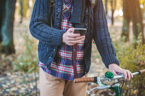 Close up of young hipster man in scarf with smartphone and bicycle texting message in autumn park