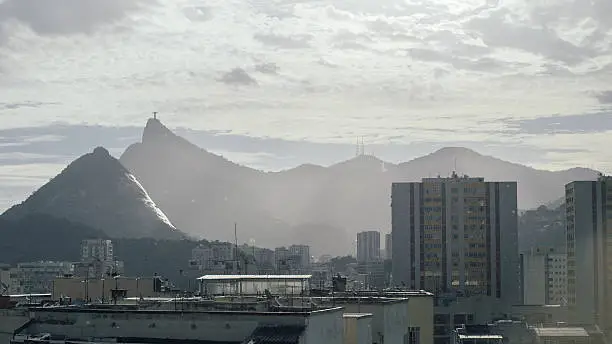 View on urban neighbourhood in Rio de Janeiro with Cristo Redentor in a far distance, on a cloudy day with sun breaking through