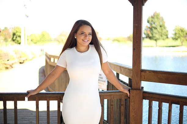 Smiling young Caucasian woman in shorts and a white shirt sits on wooden stairs near a red brick wall on a sunny day