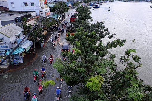 Ho Chi Minh City, Viet Nam - October 18, 2016: Awful flooded street at Asian city, crowd of people ride motorcycle wade in water from tide on road, climate change make sea level rise, Vietnam