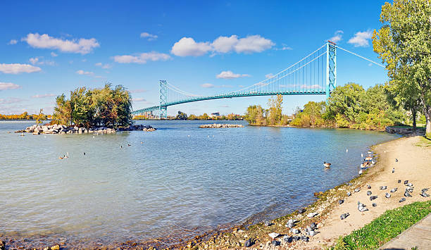 Waterfront Park Views of Ambassador Bridge on the Detroit River Beautiful late Autumn day at the Windsor, Ontario, Canada waterfront park on the Detroit River, looking at the Ambassador Bridge crossing from Windsor, Ontario, Canada to Detroit Michagan. clear sky usa tree day stock pictures, royalty-free photos & images