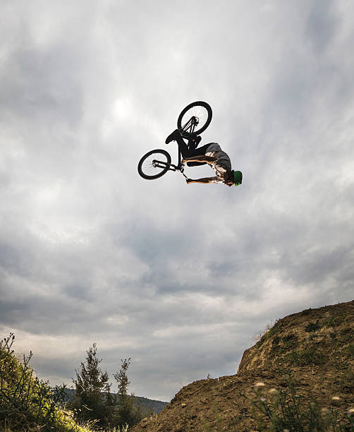 горный велосипед всадника практикующих сальто двигаться против неба. - bmx cycling bicycle cycling backflipping стоковые фото и изображения