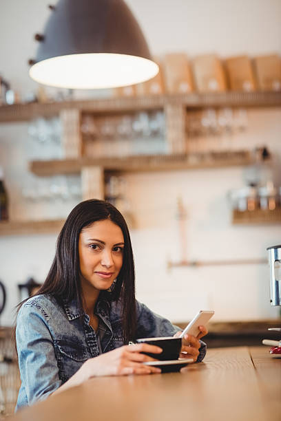istock Young woman holding mobile phone and coffee cup 617738640
