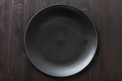 top view of one black plate on dark brown table