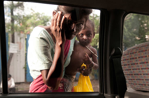 Mumbai, India - Jul 14 2010: A mother, begging for money with her daughter, flag down passengers in vehicles at a traffic light on a Mumbai street.