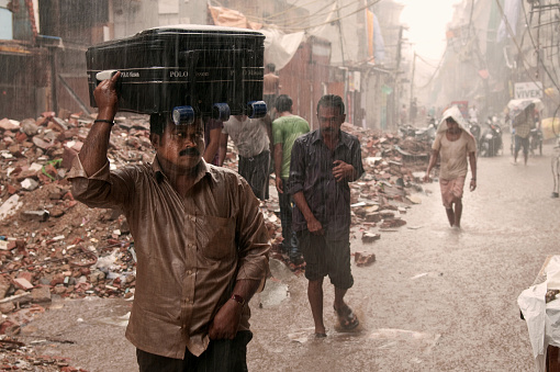 New Delhi, India - Aug 14 2010: A man uses a suitcase for cover, as annual monsoon rains in India flood a street undergoing renovations in the lead up to the Commonwealth Games.