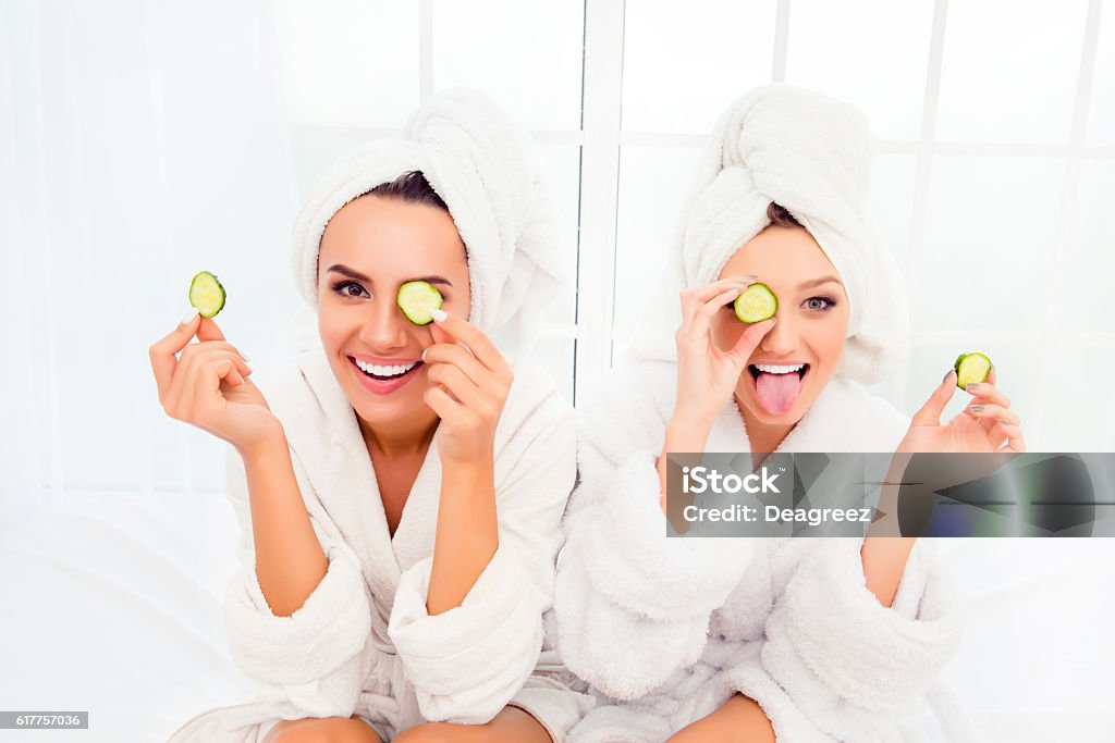 Comic young sisters after shower making mask with cucumber Cucumber Stock Photo