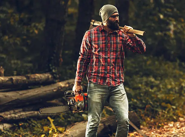 Lumberjack worker standing in the forest with axe and chainsaw