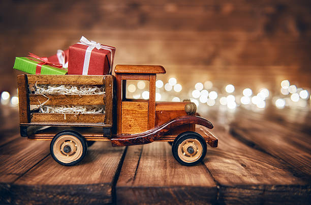 Merry Christmas and Happy Holidays! Gifts boxes presents on toy car and Christmas garland lights on old dark wooden rustic background. Celebration concept.