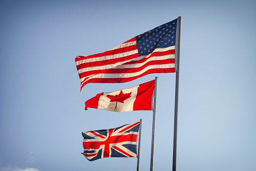 American Flag, Canadian Flag and Flag of Great Britain on blue sky.