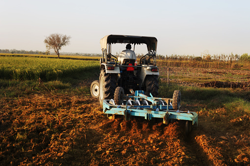 Farmer working in the field using tractor and harrow. 