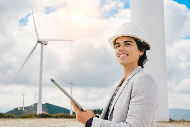 souriant vert indestry ingénieur femme tenant tablette avec casque de sécurité - engineer wind turbine alternative energy energy photos et images de collection