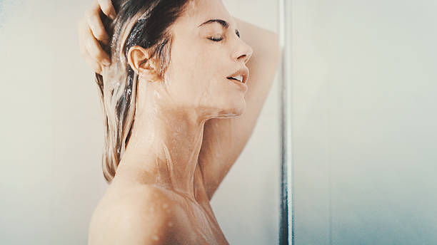 Woman under a relaxing shower. Closeup side view of mid 20's attractive woman taking a relaxing shower after a long stressful day. She's just standing under the waterflow without any soap or shampoo. washing hair stock pictures, royalty-free photos & images