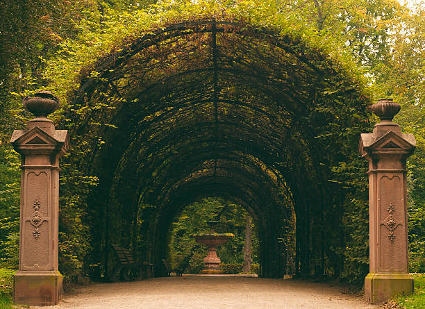 A green tunnel leading to an ornate stone fountain, in Parc de l'Orangerie Strasbourg, France.