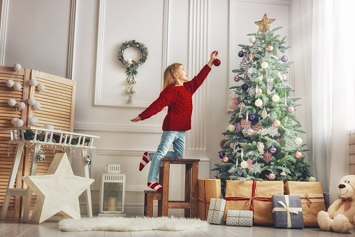 Merry Christmas and Happy Holidays!  Cute little child girl is decorating the Christmas tree indoors.