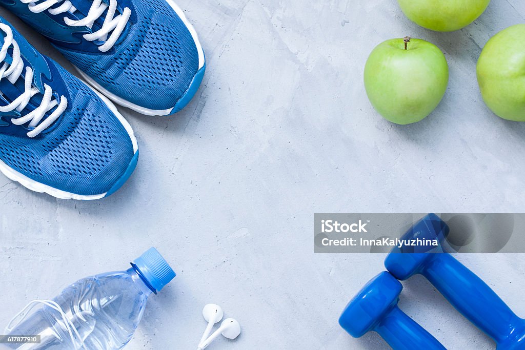 Flat lay sport shoes, dumbbells, earphones, apples, bottle of water Flat lay sport shoes, dumbbells, earphones, apples, bottle of water on gray concrete .background. Concept healthy lifestyle, sport and diet. Selective focus. Flat lay shot of .Sport equipment. Wellbeing Stock Photo