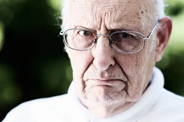 This elderly gentleman glares at the camera over his spectacles, frowning in disapproval. A classic Grumpy Old Man!