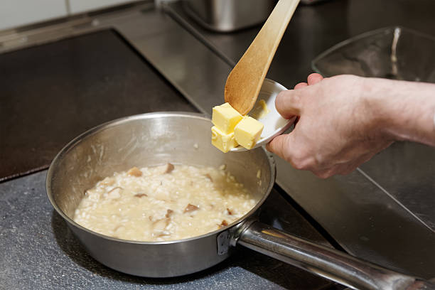 chef is putting butter to risotto - commercial kitchen restaurant retail stainless steel imagens e fotografias de stock