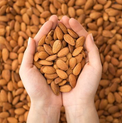 Young woman hands holding almonds on background