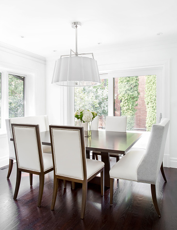 Vertical image of modern dinning table and six chairs and white chandelier. Double sized banquet chairs at the head of the table.