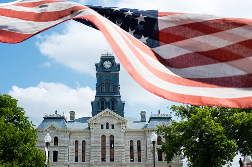 Limestone courthouse with clock tower in the small Texas town of Granbury, behind the American flag 