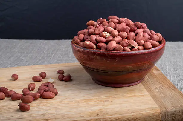 Old wooden bowl filled with raw nuts peanut is on the table on a wooden stand
