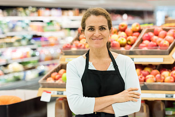 成熟した女性の食料品店の労働者 - supermarket sales clerk grocer apron ストックフォトと画像