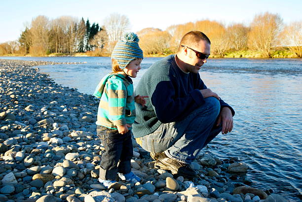 Father with Child by the River A Father squats beside his child by the river in late winter sunshine. motueka stock pictures, royalty-free photos & images