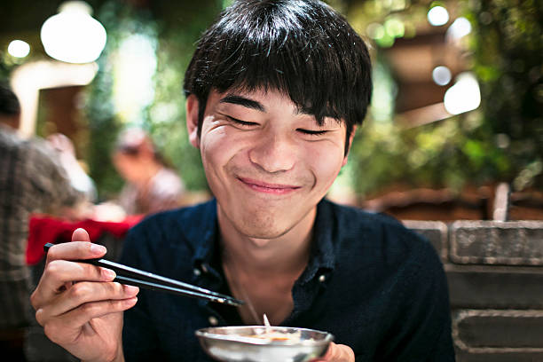 lustige junge japanische mann essen mit essstäbchen - eating men food chopsticks stock-fotos und bilder