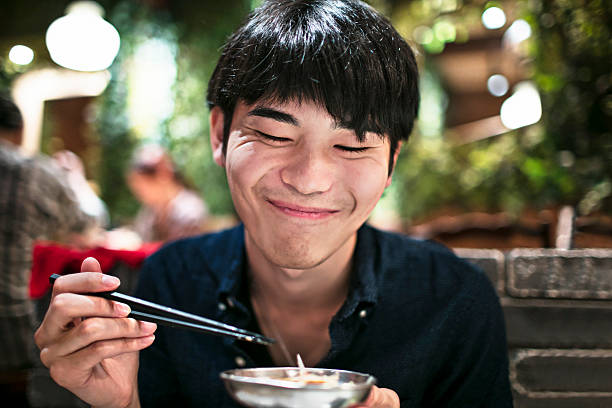 drôle de jeune japonais mangeant à l’aide de baguettes - eating men food chopsticks photos et images de collection