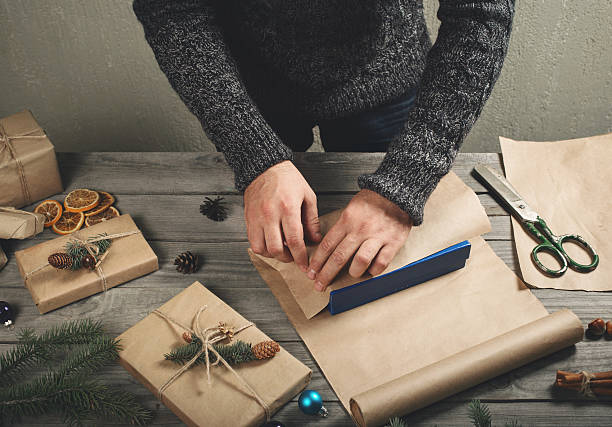 istock Male hands wrap Christmas gift on wooden table 618036356