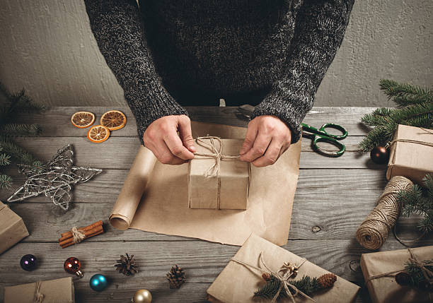 istock Male hands wrapping xmas present on wooden table 618036474