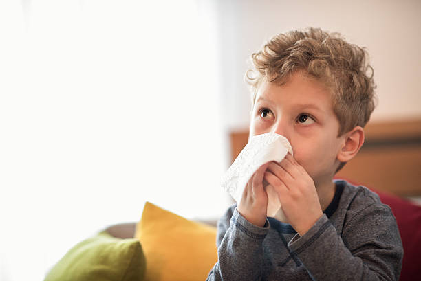 Little boy blowing nose Little boy with flu virus sitting on the sofa and wiping his nose with a napkin. Bright light is breaching throught the window in the background. blowing nose photos stock pictures, royalty-free photos & images