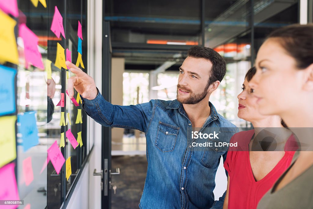 Three businesspeople discussing and planning concept Three businesspeople discussing and planning concept. Front of glass wall marker and stickers. Startup office. Adhesive Note Stock Photo