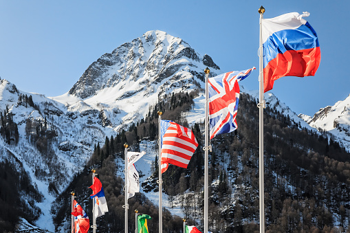National flags of Russia, UK, USA and other countries waving in the wind as a friendship and collaboration symbol on snowy mountains and blue sky background. Various flattering national flags on flagpoles